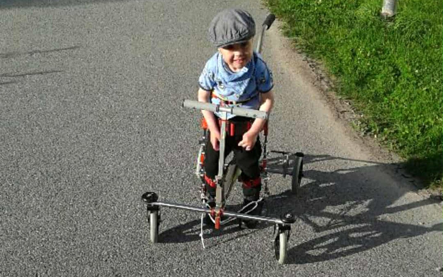 Ein kleines Kind nutzt das Mobilitätshilfsmittel NF-Walker im Freien und übt unterstütztes Gehen auf einer asphaltierten Straße mit breiter Radbasis für Stabilität.