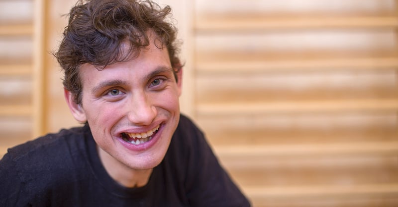 Lächelnder junger Mann mit lockigem Haar vor einer Sprossenwand.