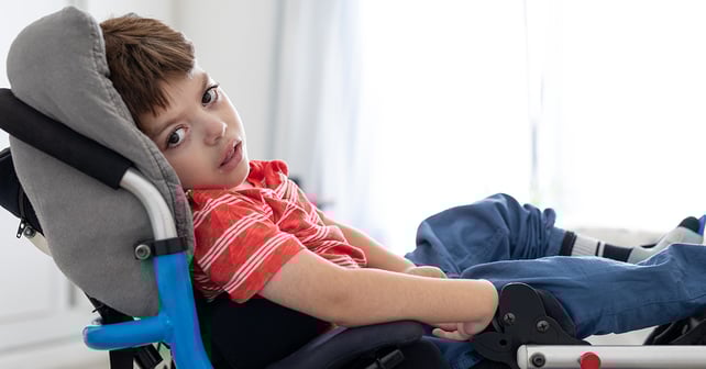 Young boy with cerebral palsy in his wheelchair looking at the camera.