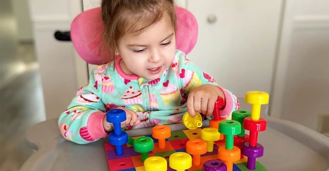 En jente sitter i Squiggles-sittesystemet og deltar i en aktivitet ved bordet.