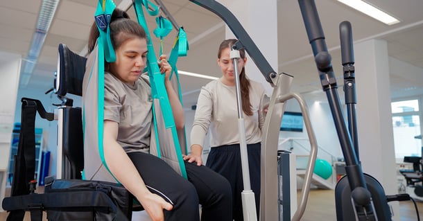 En person överförs säkert till en Innowalk med hjälp av en lyft, assisterad av en vårdgivare.
