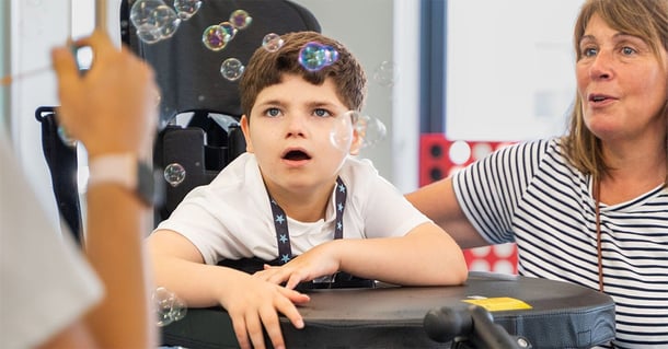 A young boy in a Innowalk watches bubbles with wonder during a playful activity.