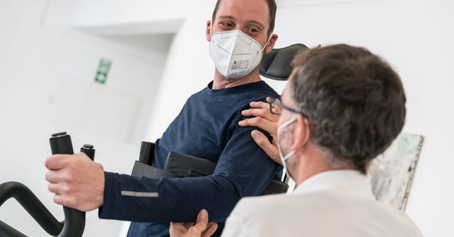 Man with face mask in Innowalk and their therapist 