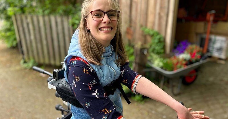 En kvinna vid namn Charlotte sitter på en Xplore i en solig utomhusmiljö omgiven av gröna växter.