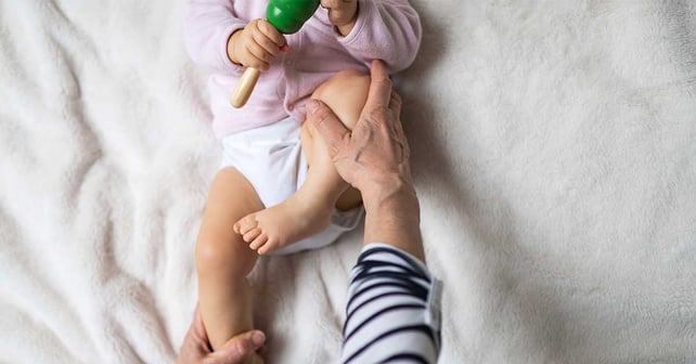 Little baby receiving osteopathic treatment of her leg to prevent hip dysplasia by pediatric physiotherapist.