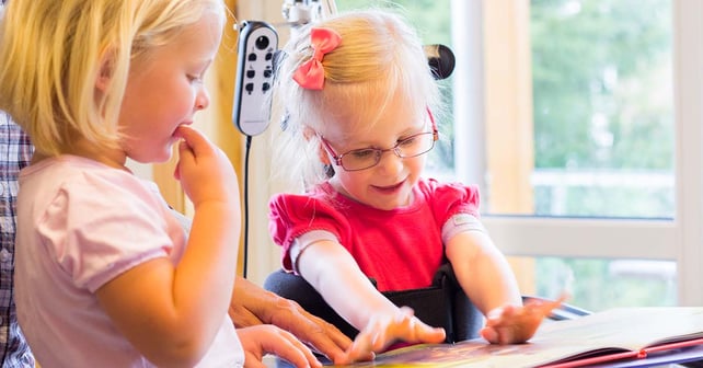 Flicka med cerebral pares läser bok med kompis i Innowalk