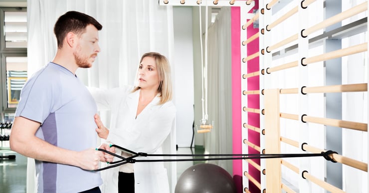 Mann som trener med strikk i ribbevegg, instruert av kvinnelig lege. Fysisk aktivitet kan ha store helsefordeler for deg med MS.