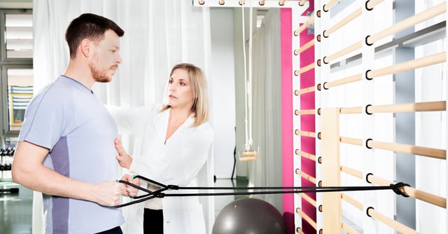 Mann som trener med strikk i ribbevegg, instruert av kvinnelig lege. Fysisk aktivitet kan ha store helsefordeler for deg med MS.