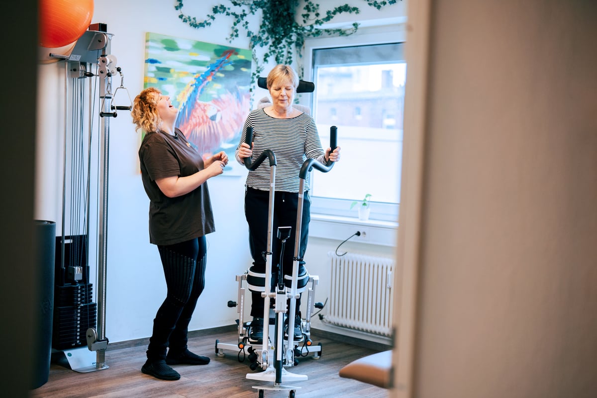 Eine Frau steht in ihrem Innowalk Pro und lacht mit ihrer Physiotherapeutin