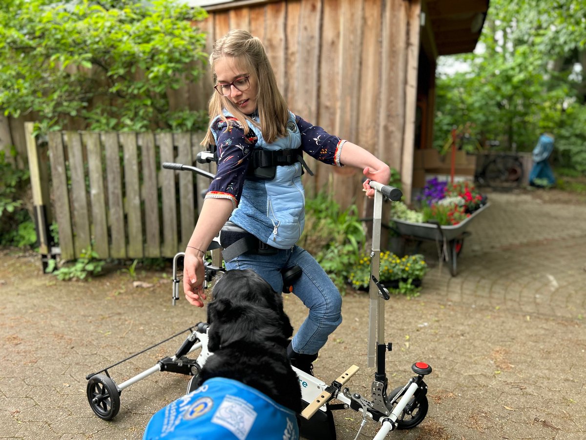 En närbild av Charlotte, en kvinna med ett levande leende och uttrycksfulla ögon, som går utomhus i Xplore en solig dag och sträcker sig efter sin hund.