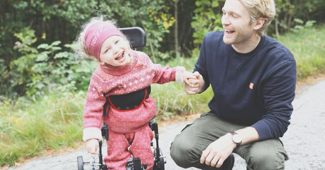 Leende flicka i rosa kläder går i NF-Walker och håller sin fars hand.