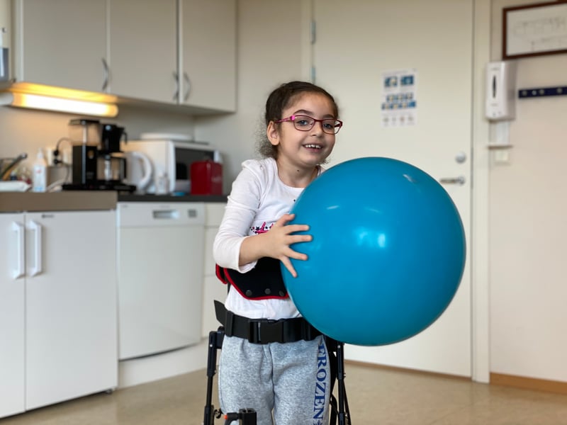 Ung flicka som leker med stor blå boll när hon står i NF-Walker