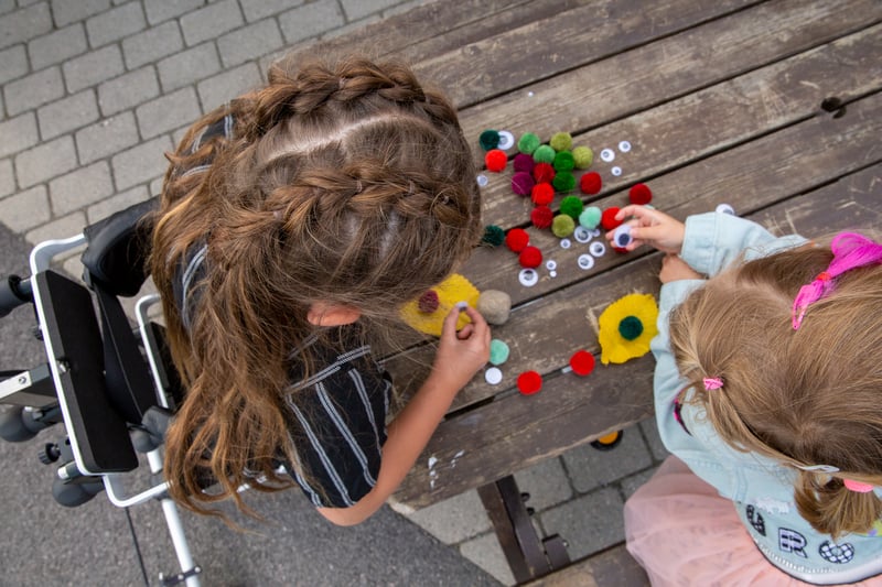 young girl stands in her xplore at a table playing with her friend