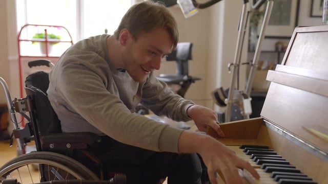 Junger Mann spielt seine Gitarre, während er in seinem Rollstuhl sitzt