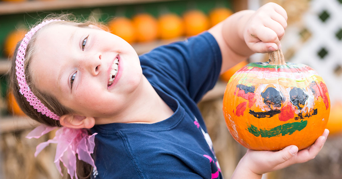 Smiling little girl showing her painted pumpkin.